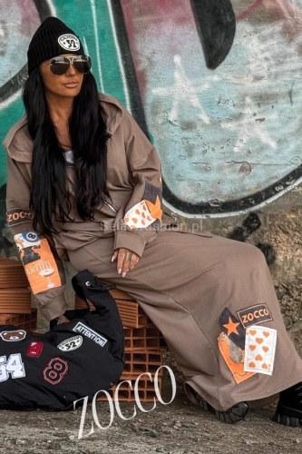 Komplet maksi od firmy Zocco składający się z bluzy na zamek, z kapturem i spódnicy na gumie z wiązaniem. Cały set uszyty z materiału bawełnianego, z kolorowymi naszywkami.